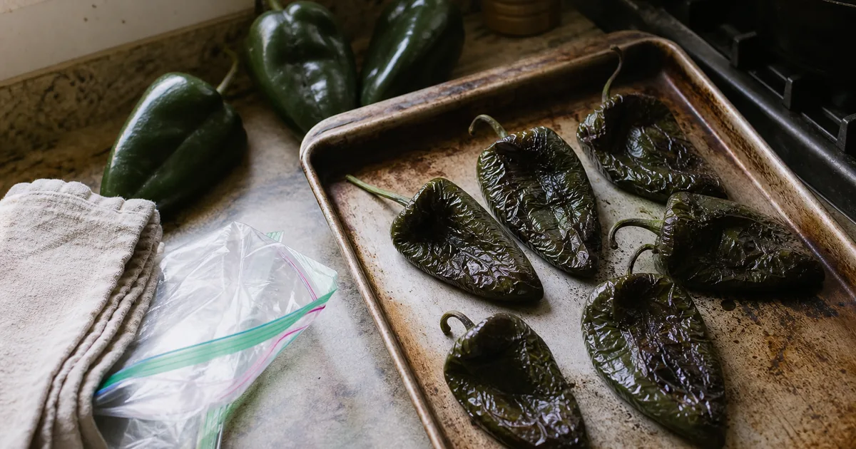 Roasted poblano peppers cooling beside freezer bags and a sheet pan